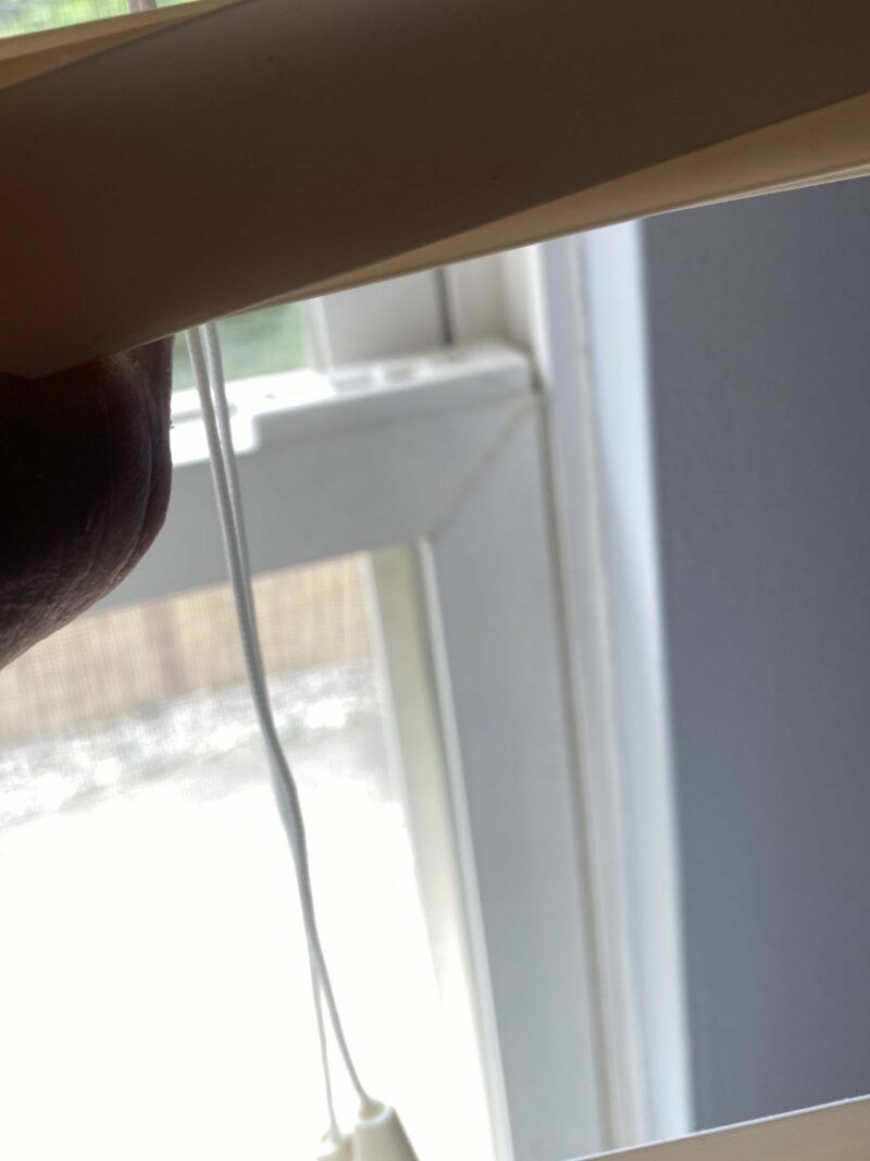 Close-up of a hand holding a white cord beside a bright window