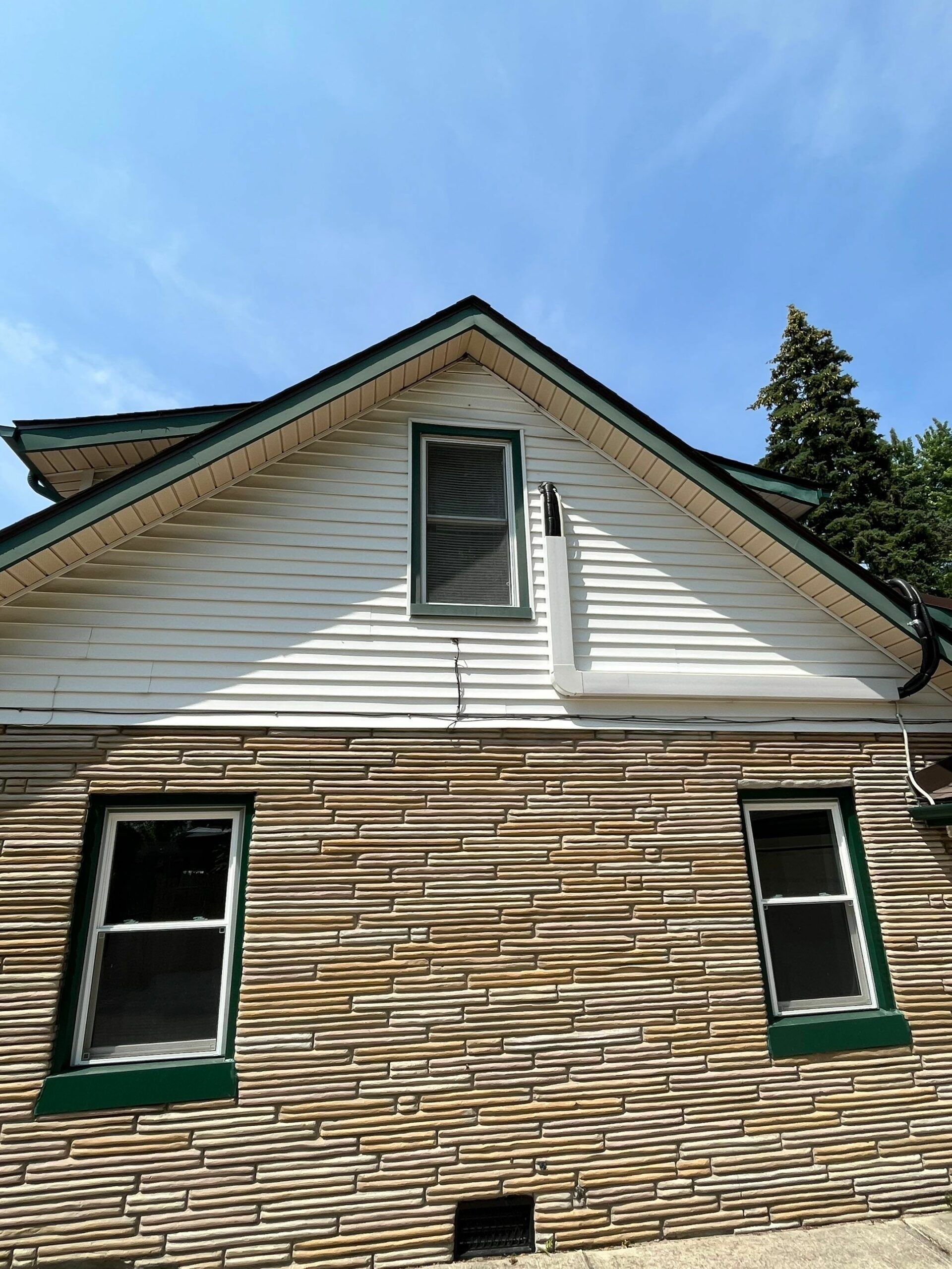 House exterior with white gable, tan shingle siding, and green-trimmed windows against a blue sky