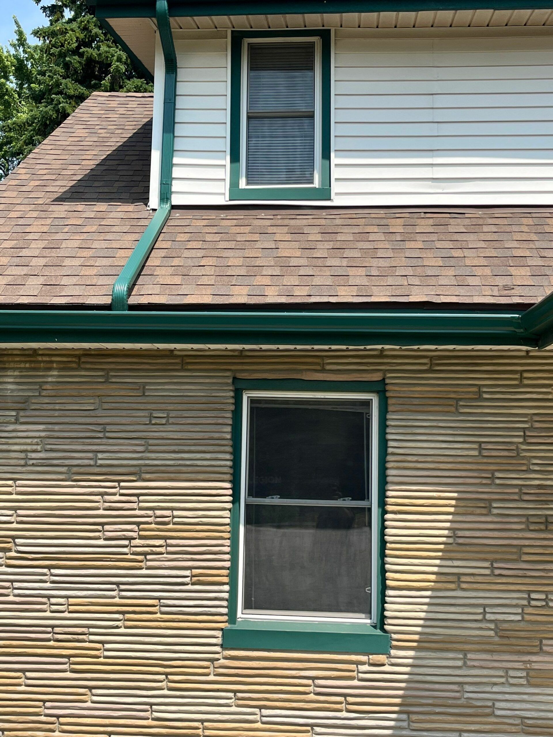 Two-story house exterior with beige siding, green trim, shingled roof, and two windows.
