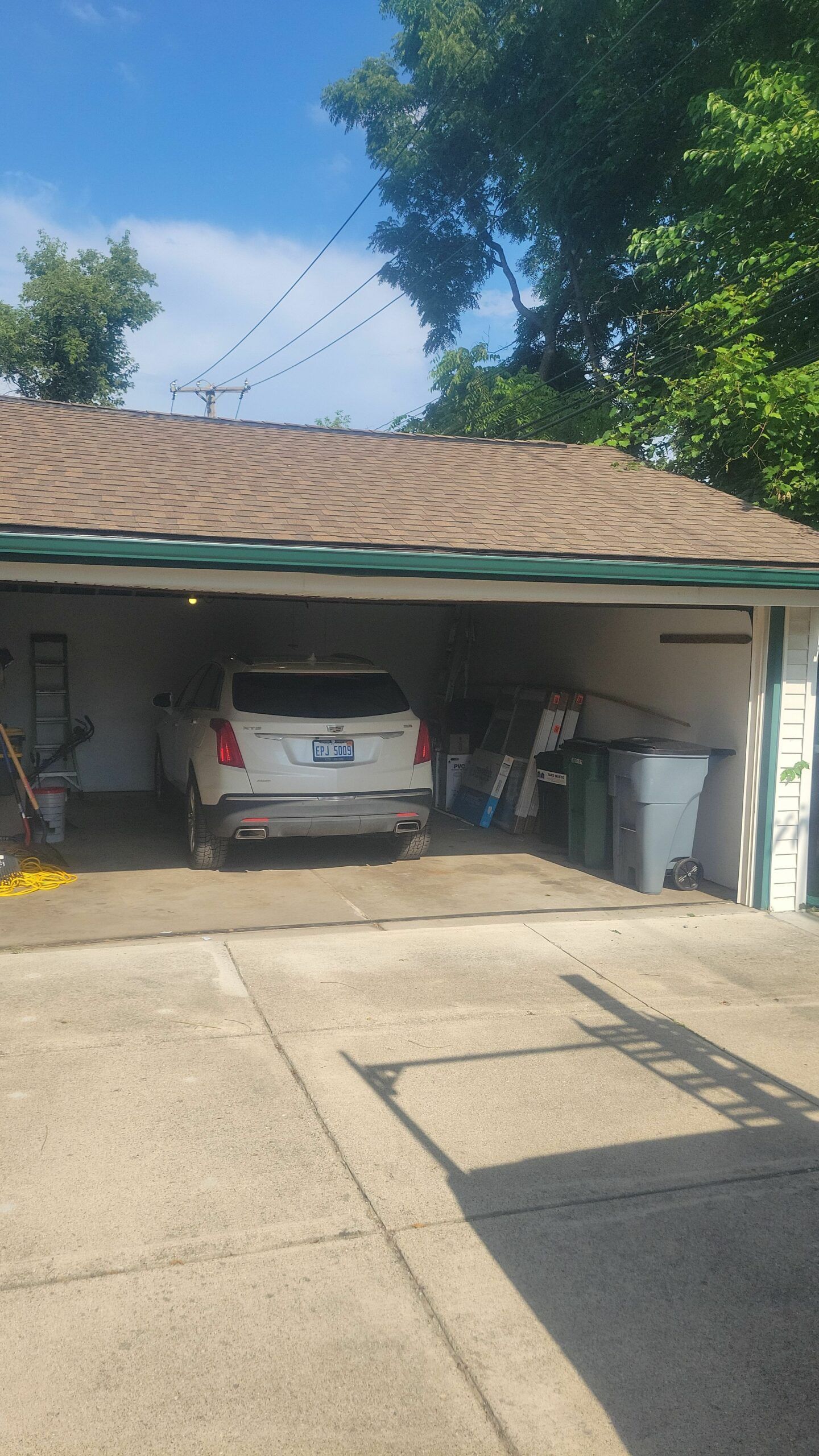 Carport with a silver SUV parked inside, green roof trim, and a concrete driveway in front.