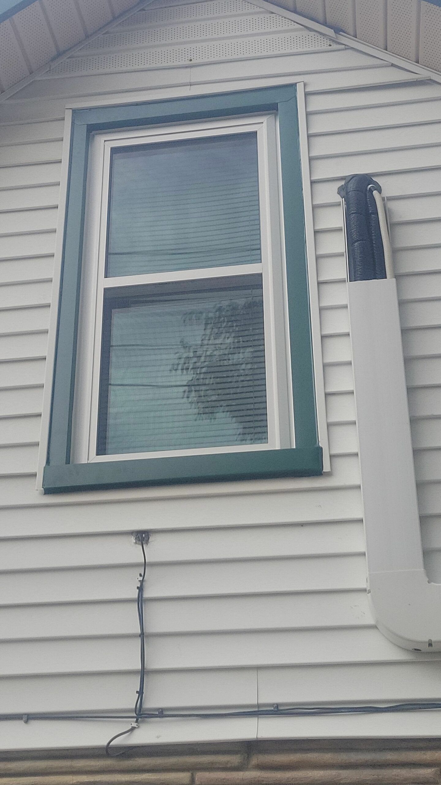 House exterior with a white-framed window and a downspout on light gray siding