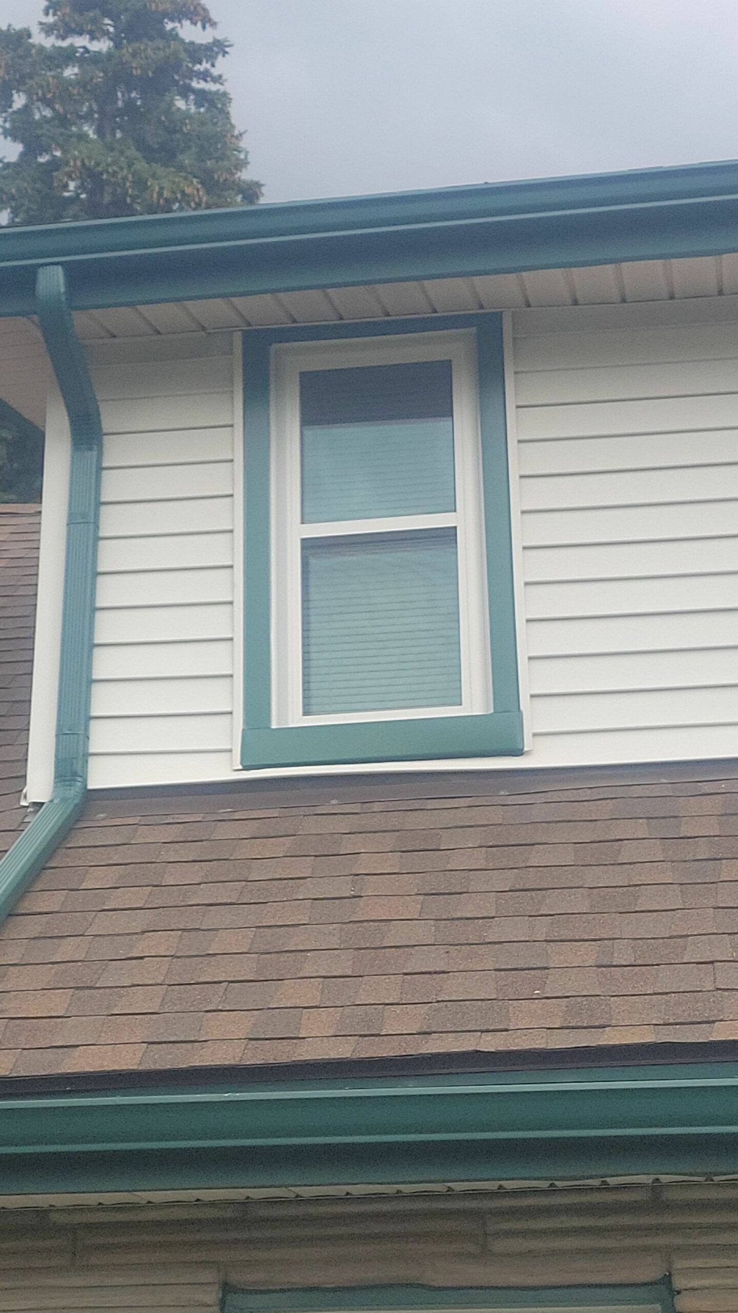 House exterior with white siding, teal trim, and a second-story window above a shingled roof