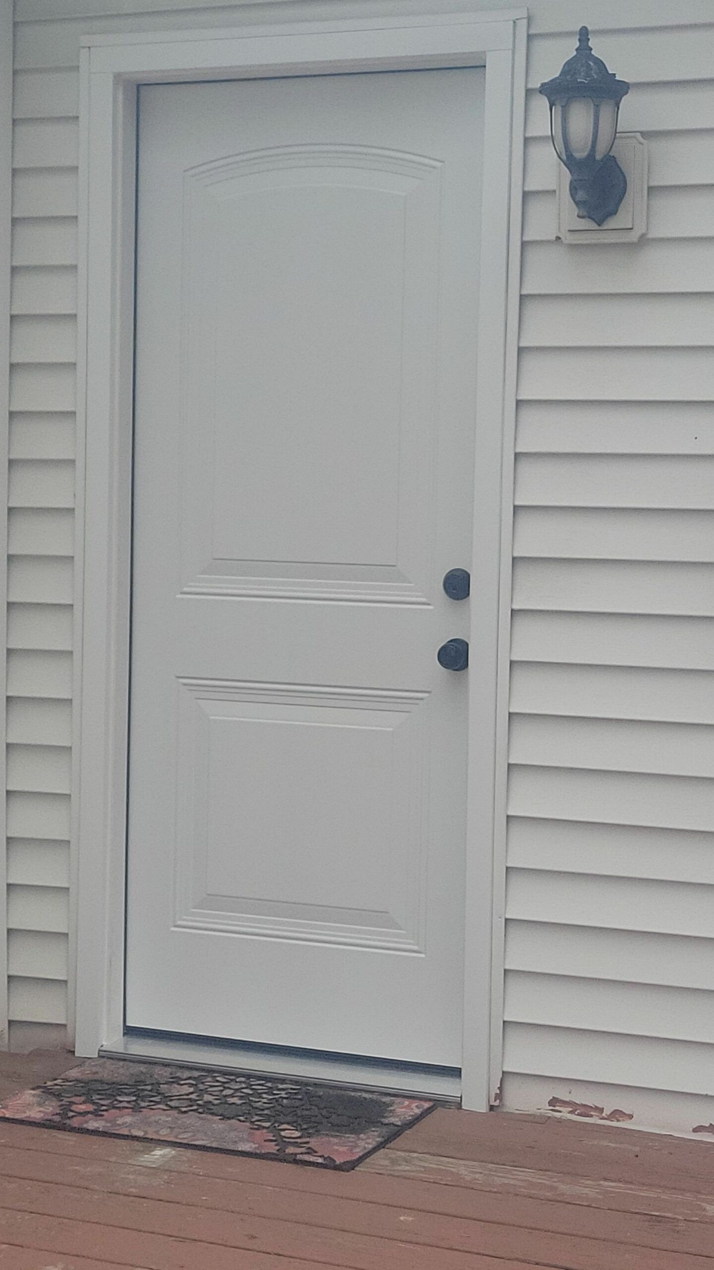 White exterior door beside wall-mounted lantern on a house siding exterior