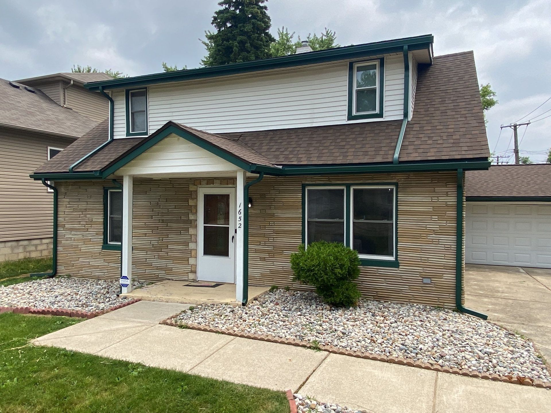 Two-story house with tan siding, white trim, and a small covered entryway beside a driveway.