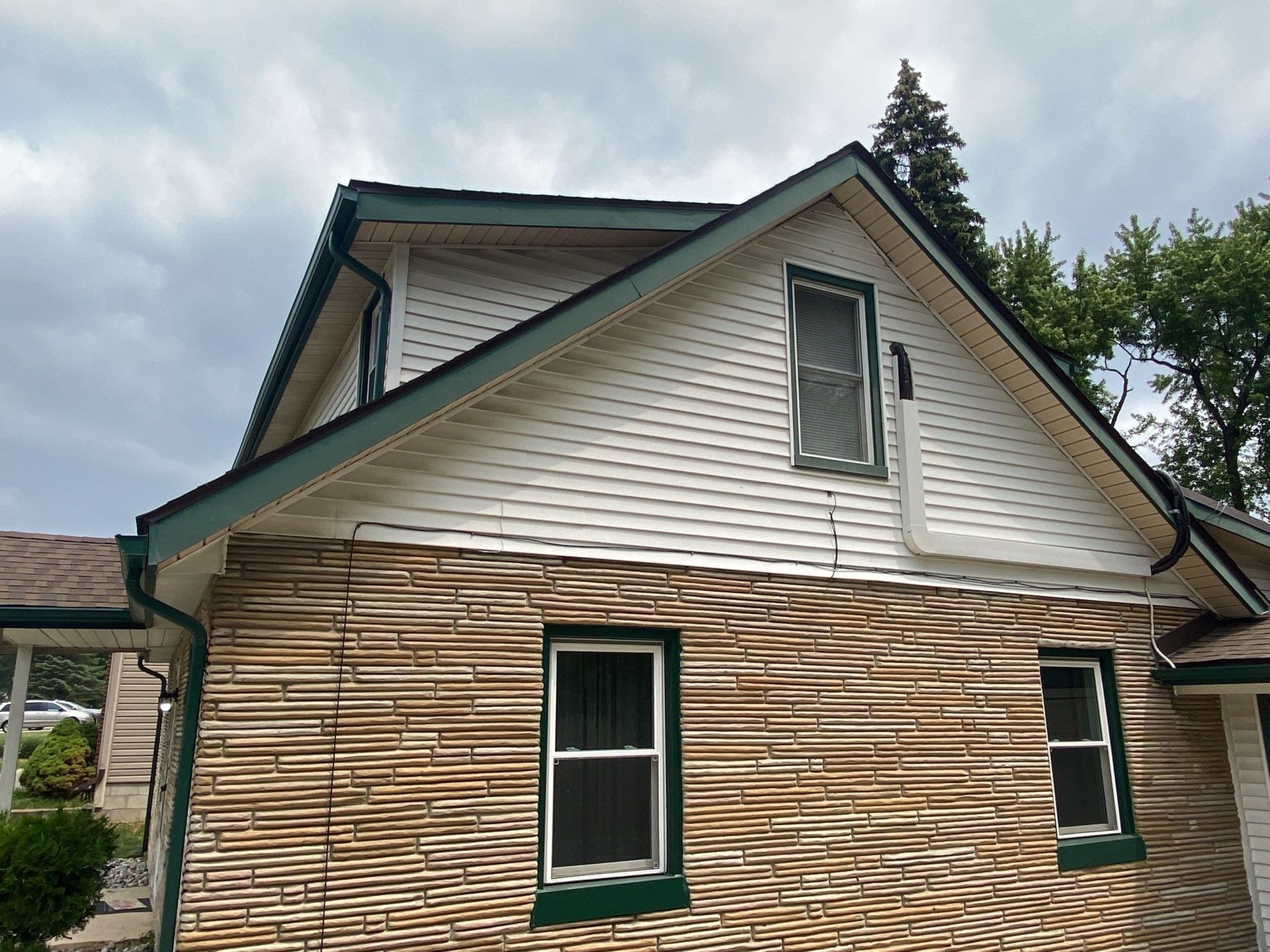 Old house with weathered siding and green-trimmed windows under a cloudy sky