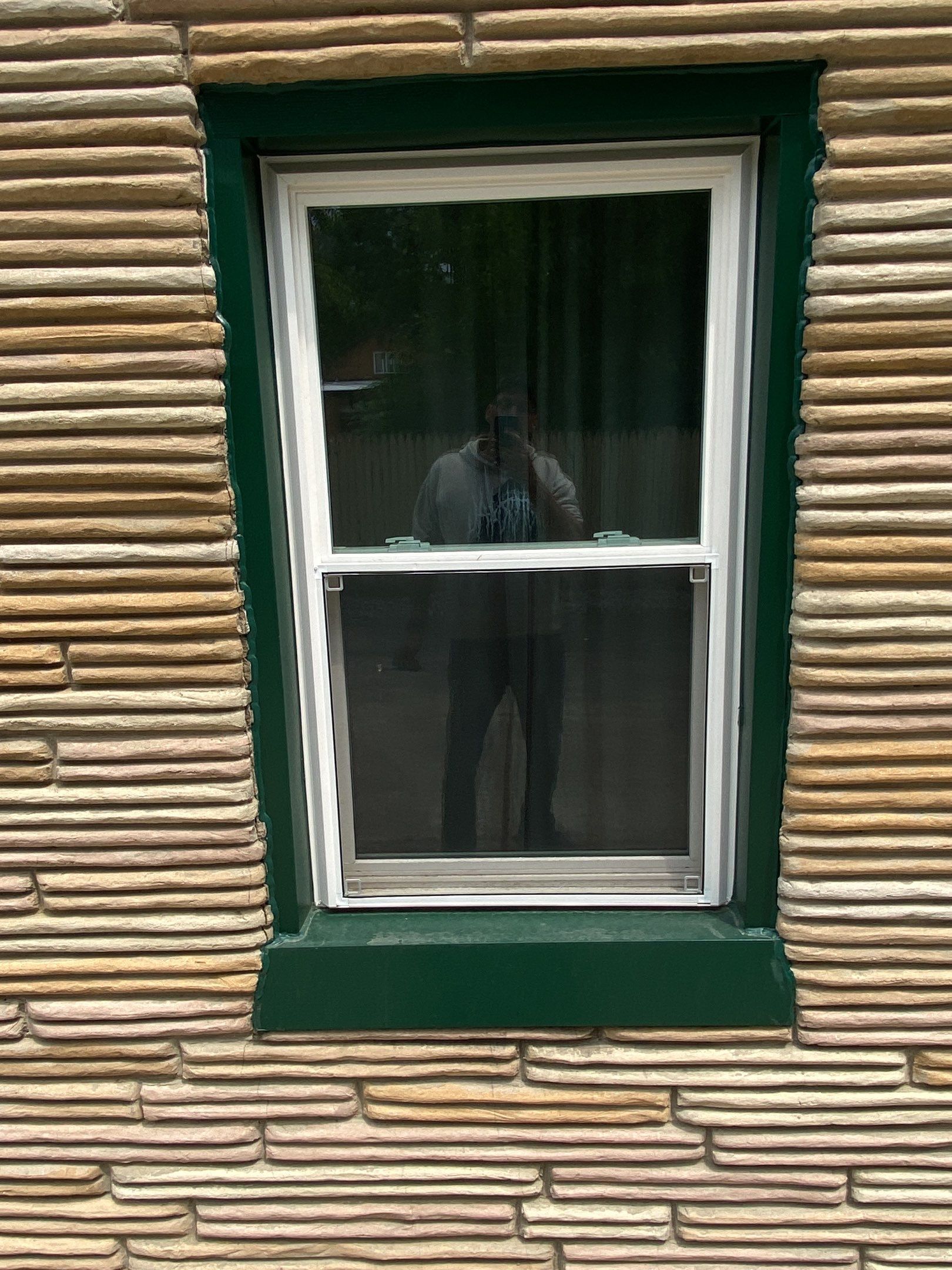White-framed window with dark green trim on a tan stone wall, reflecting a person inside