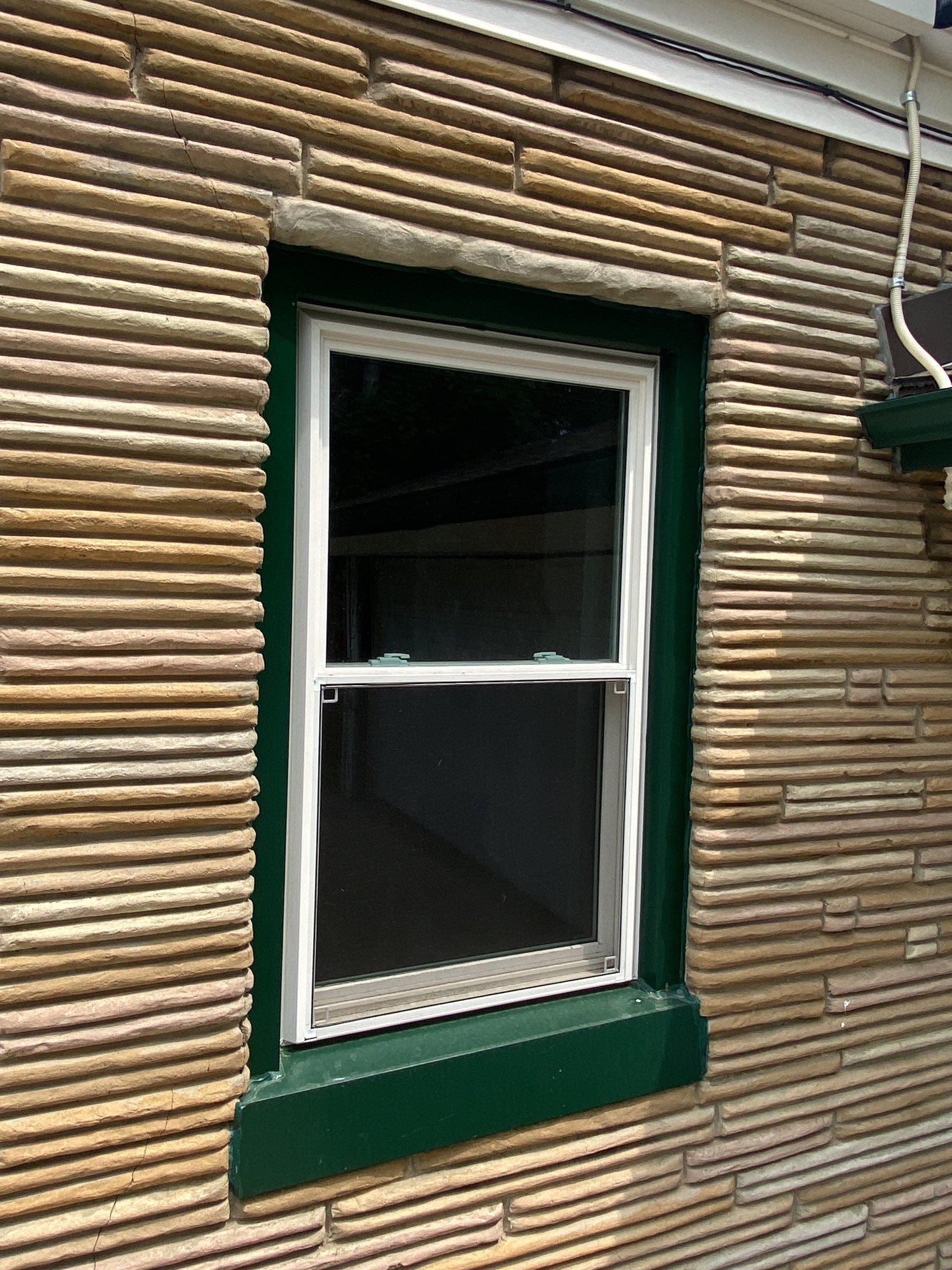 White-framed window set in a tan brick wall with a dark green sill and trim.