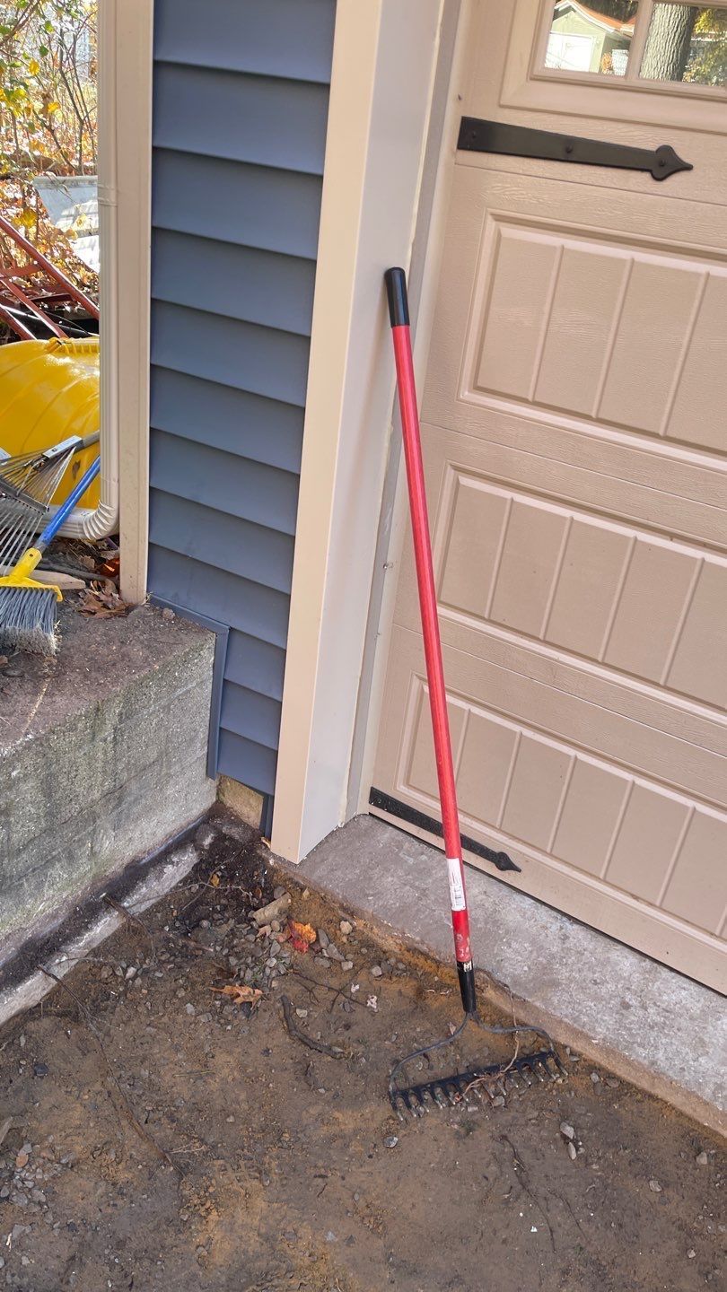Shovel leaning against garage door beside dirt and gravel work area outdoors