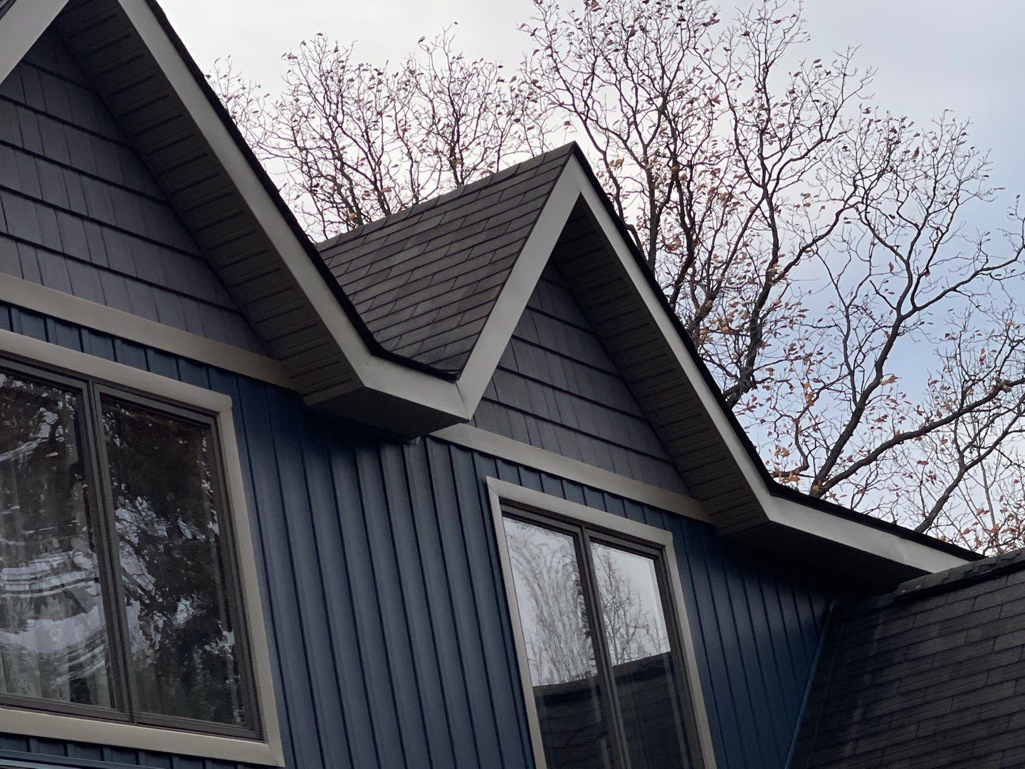 Blue house exterior with steep gables and bare tree branches against the sky