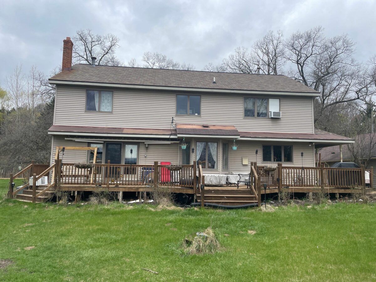 Two-story beige house with a wooden deck and lawn in front under cloudy skies