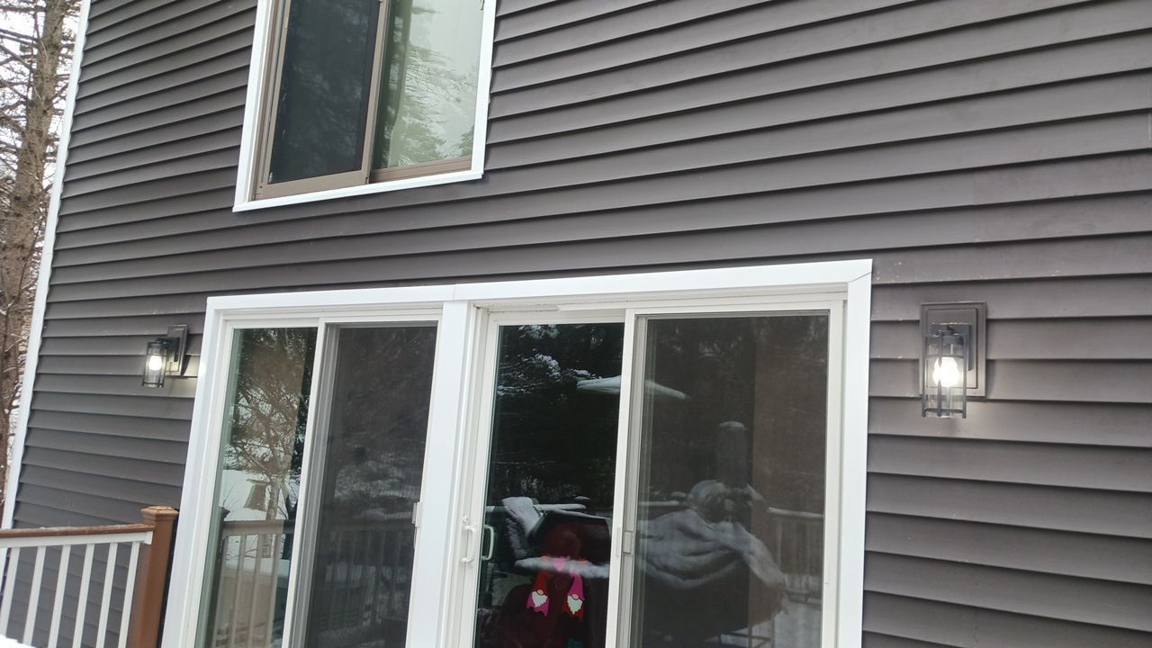 Sliding glass doors on a house exterior with dark siding and a lit wall lantern