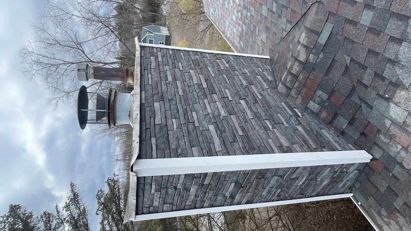 Shingled house roof with white chimney and bare trees under a cloudy sky