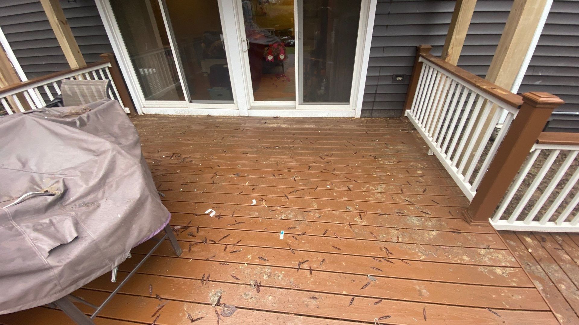 Wooden backyard deck with sliding glass doors and a covered grill, bordered by white railings.