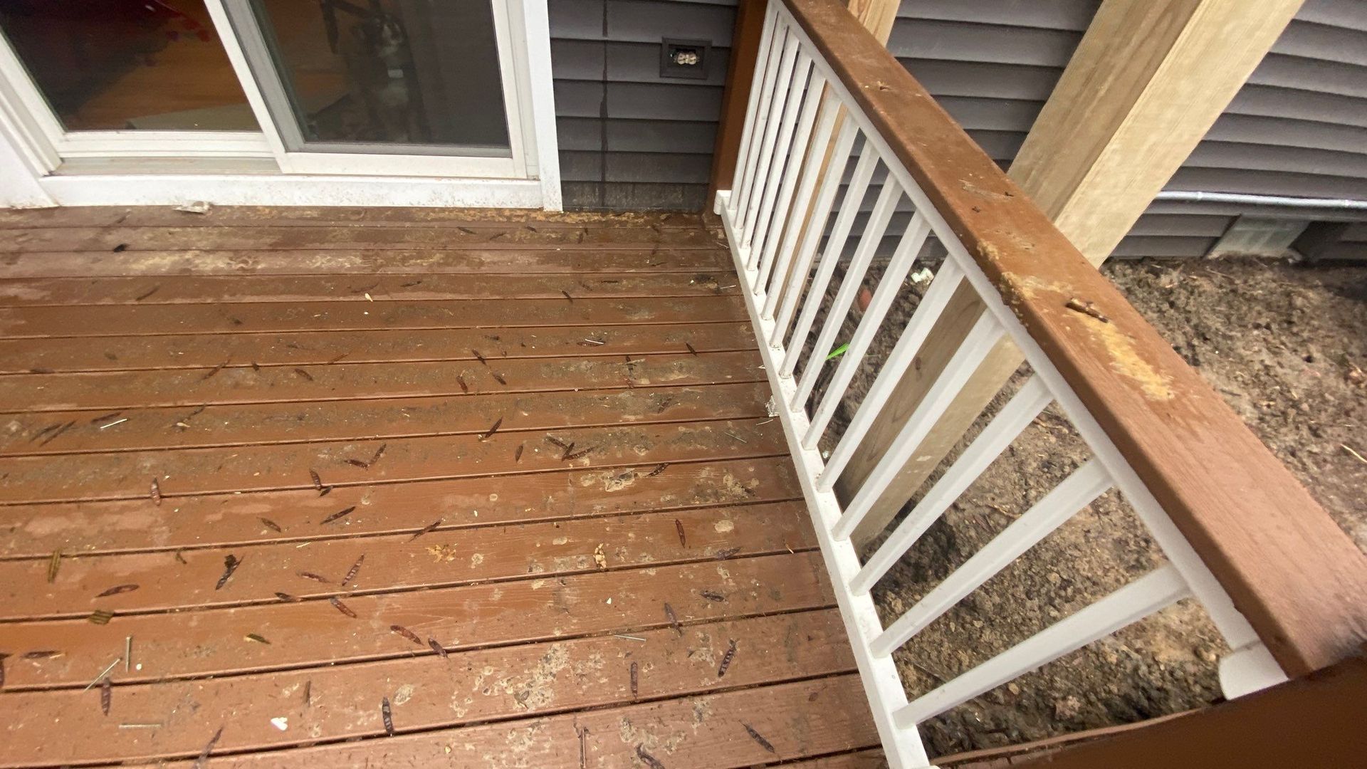 Weathered wooden porch steps with a white railing and dark brown deck boards beside a house entrance