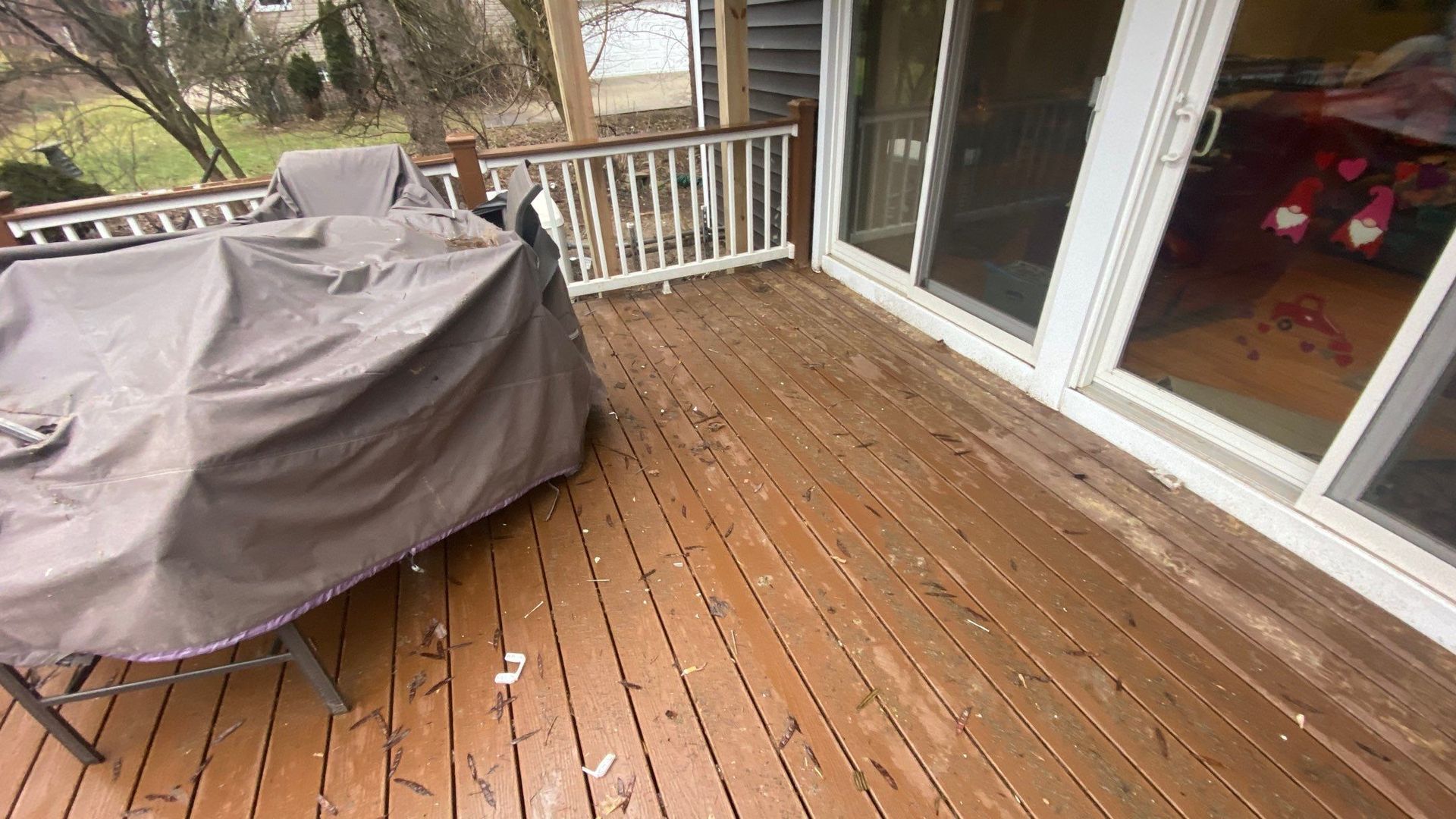 Wooden backyard deck with a covered grill, railing, and sliding glass doors leading inside.