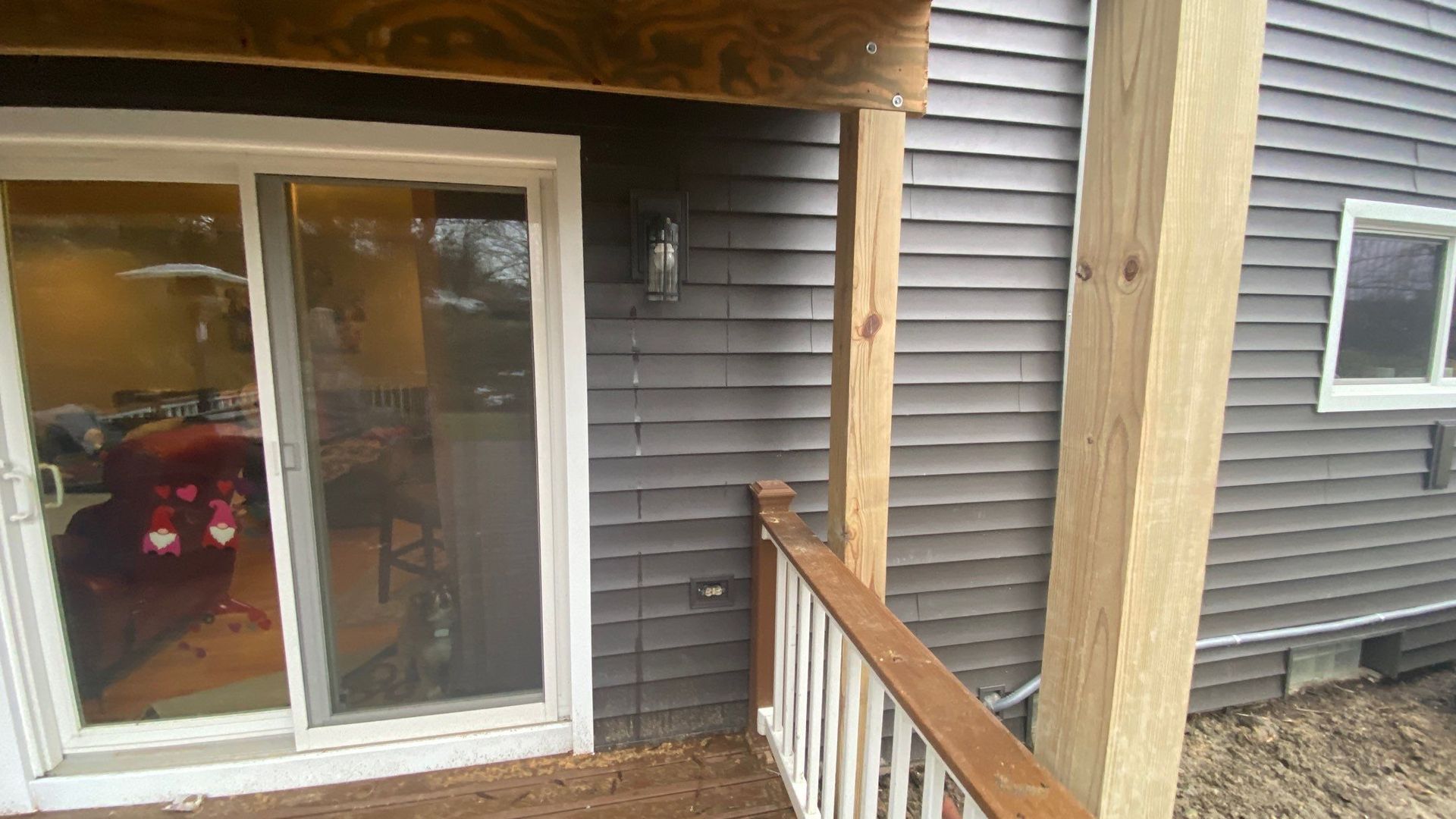 Sliding glass door to a deck with gray siding and a wooden railing; car visible inside through the glass