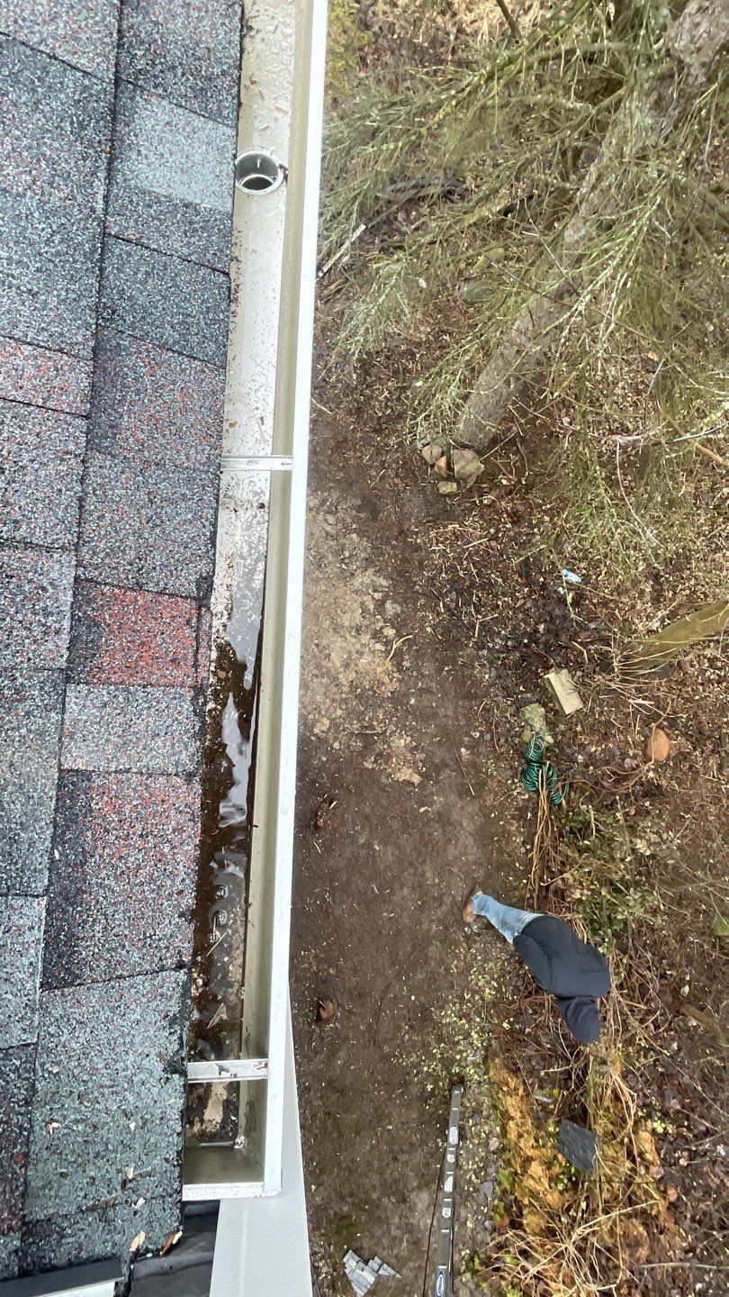 Roof edge beside a muddy yard with a gutter, downspout, and a black tarp on the ground