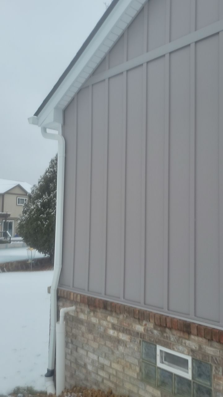 Snowy side view of a house with gray siding, brick foundation, and a small window