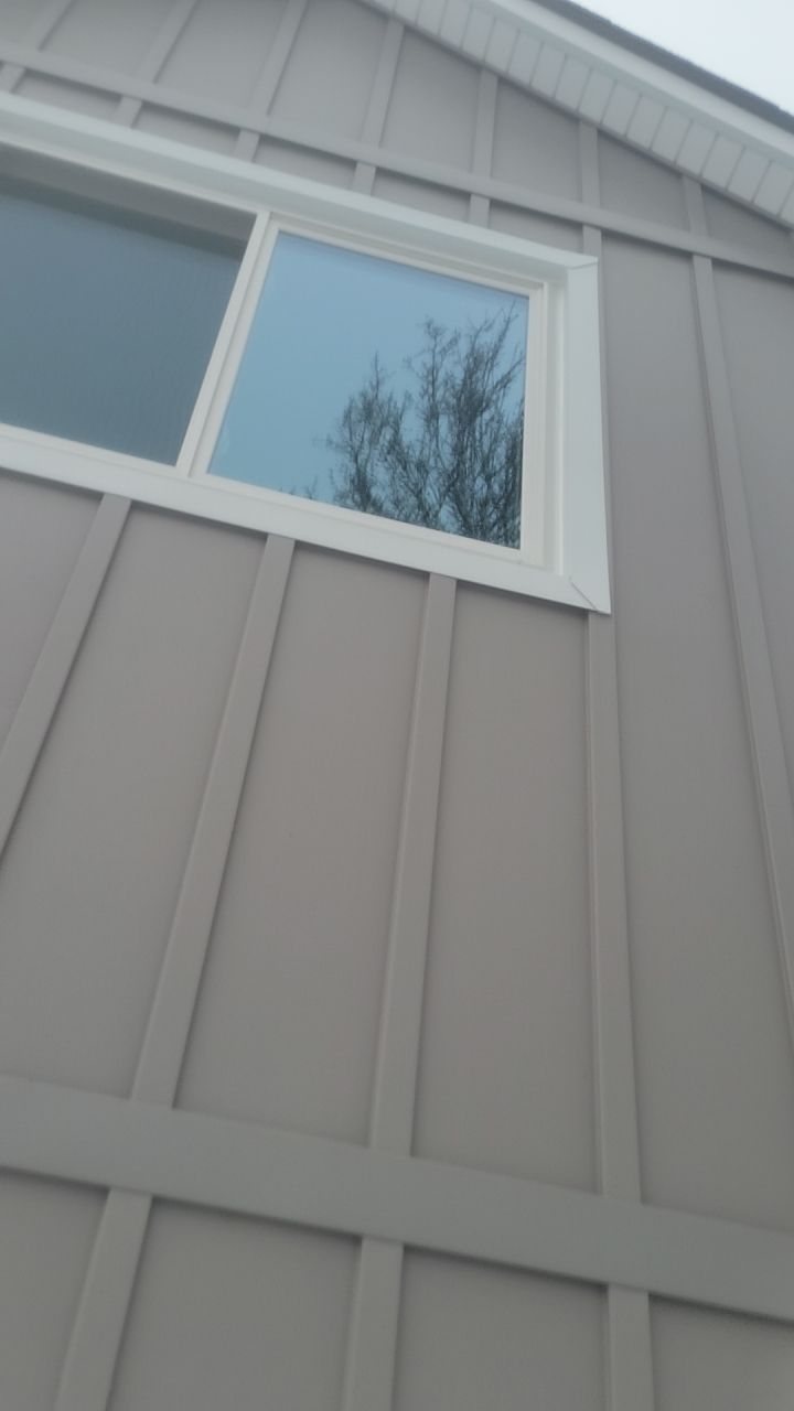 Exterior wall with a small white-framed window reflecting bare tree branches and cloudy sky