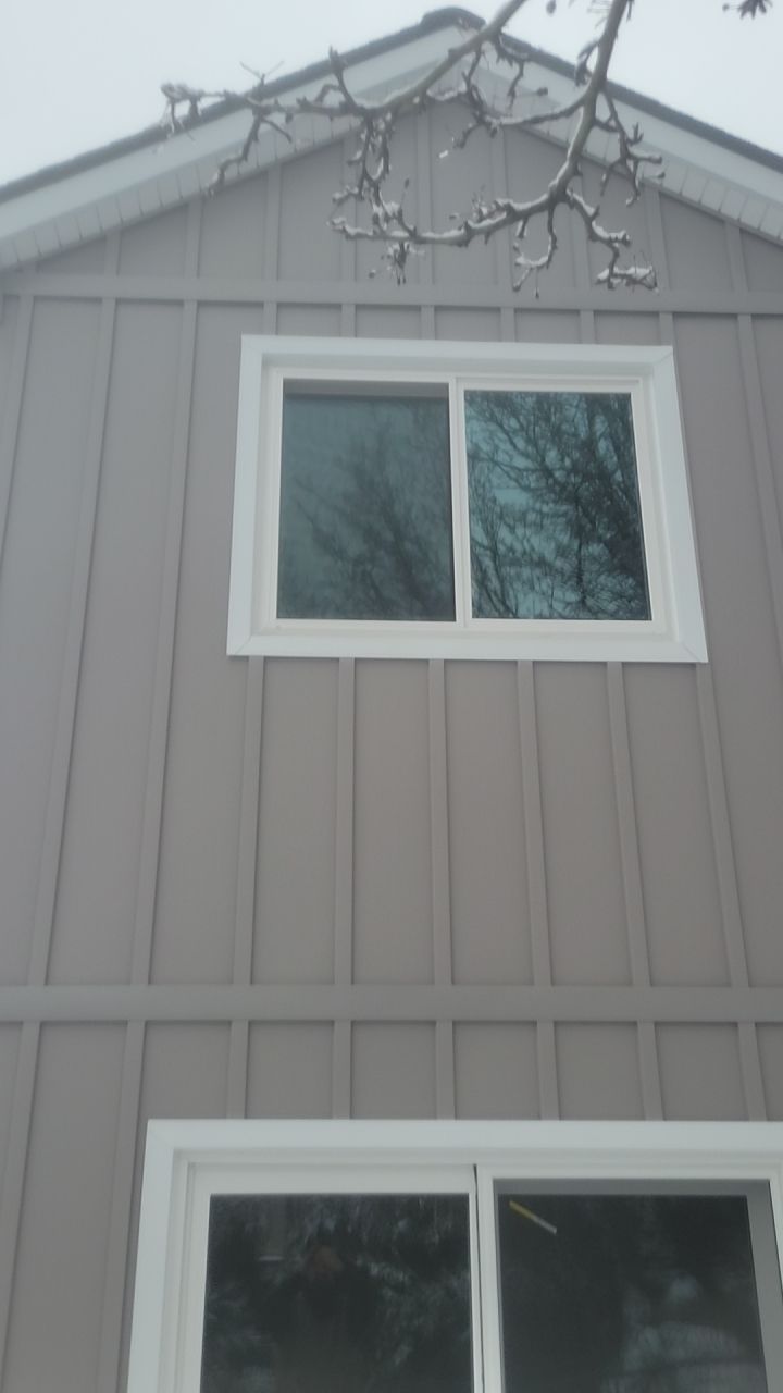 Gray house exterior with white-trimmed windows and bare tree branches overhead