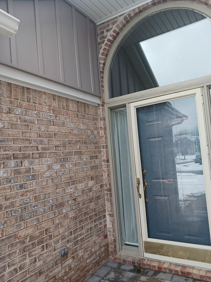 Brick front entry with arched window and glass storm door on a snowy day