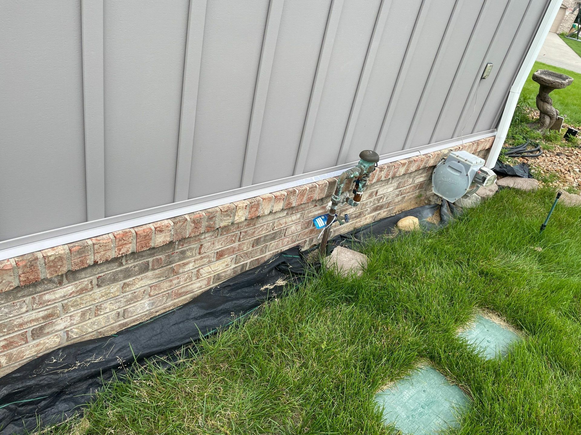 Foundation wall with a black drainage membrane beside a grassy yard and two stepping stones