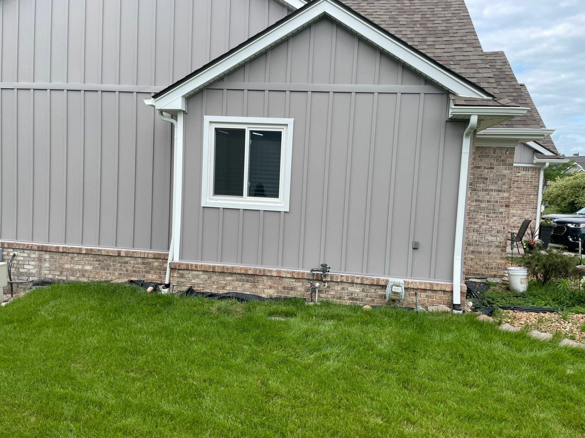 Gray house exterior with stone trim, white-framed window, and green lawn in front