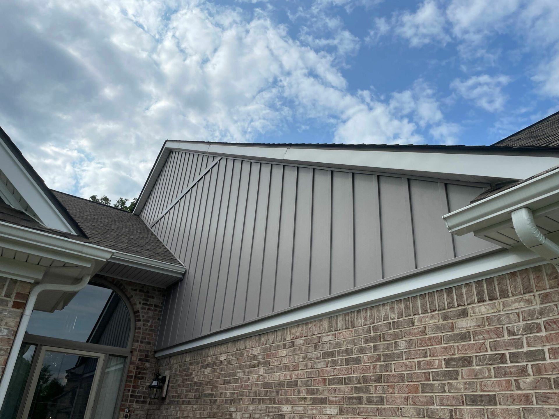 Brick house exterior with gray siding and white trim under a partly cloudy sky