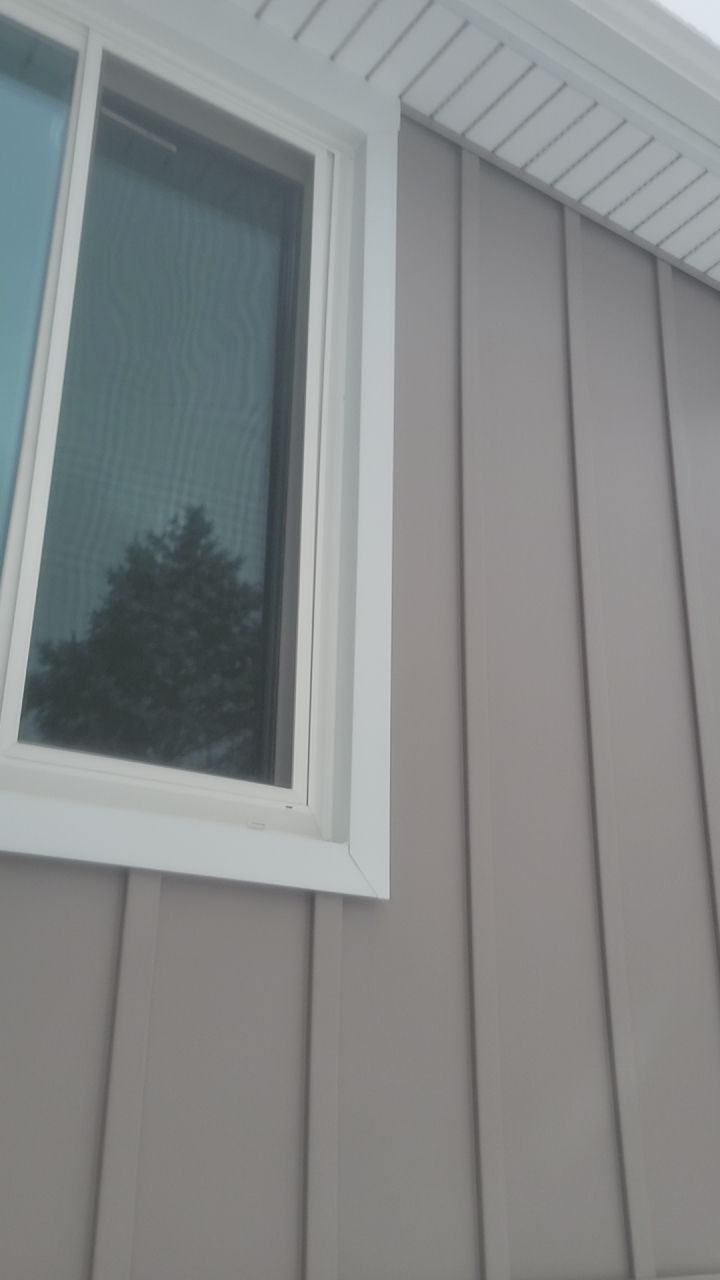 House exterior with beige siding, white-trimmed window, and roof eaves against a cloudy sky