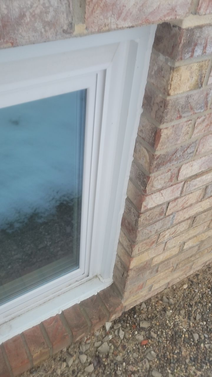 White-framed basement window set in a brick wall beside gravel ground.