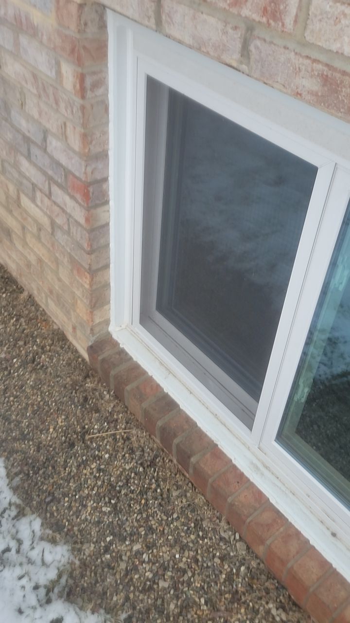 White-framed basement window in a brick wall beside gravel ground