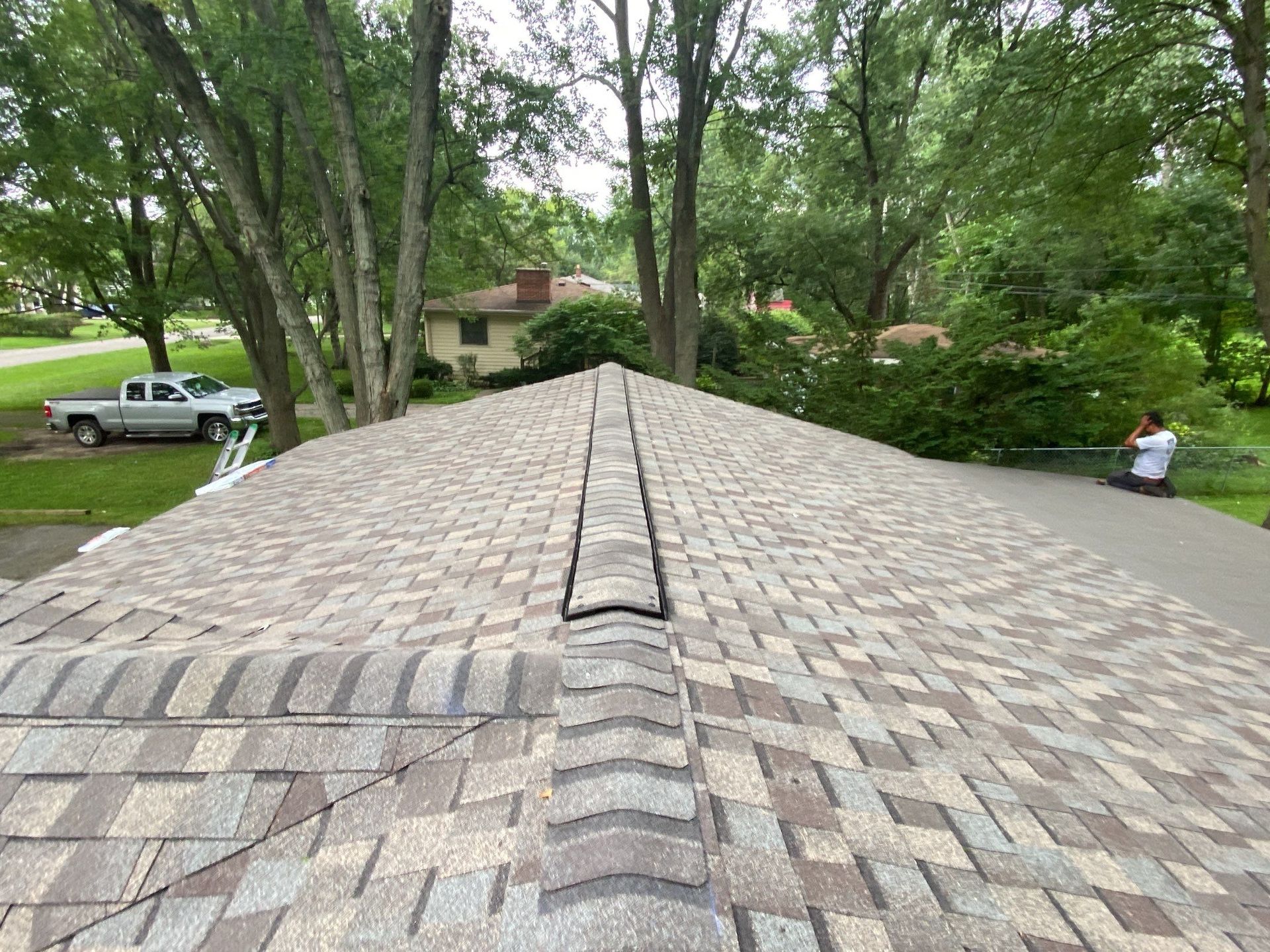 View along a shingled roof peak with trees and a driveway in the background