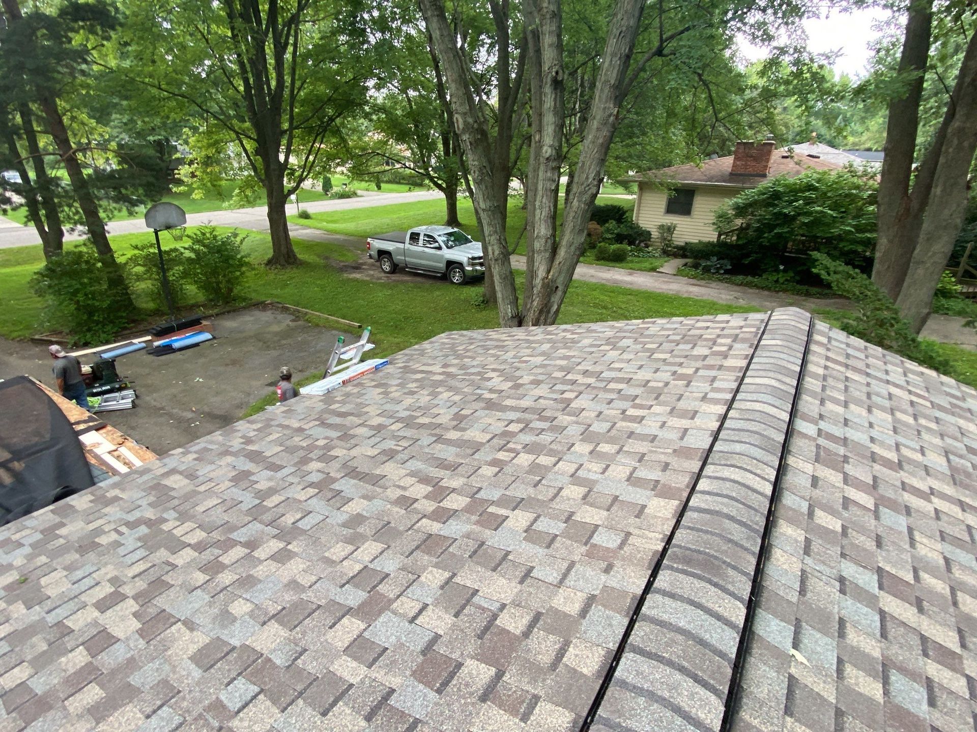 Roof with gray shingles overlooking a leafy yard, driveway, and parked car