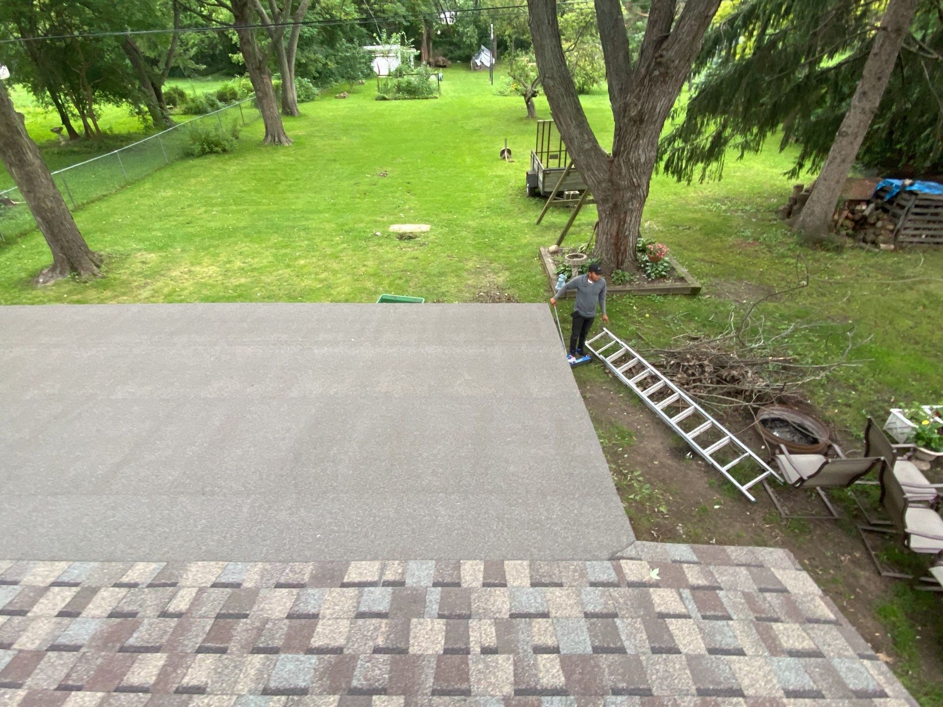 Patio overlooking a grassy yard with trees, a ladder, and outdoor chairs beside a tiled terrace.