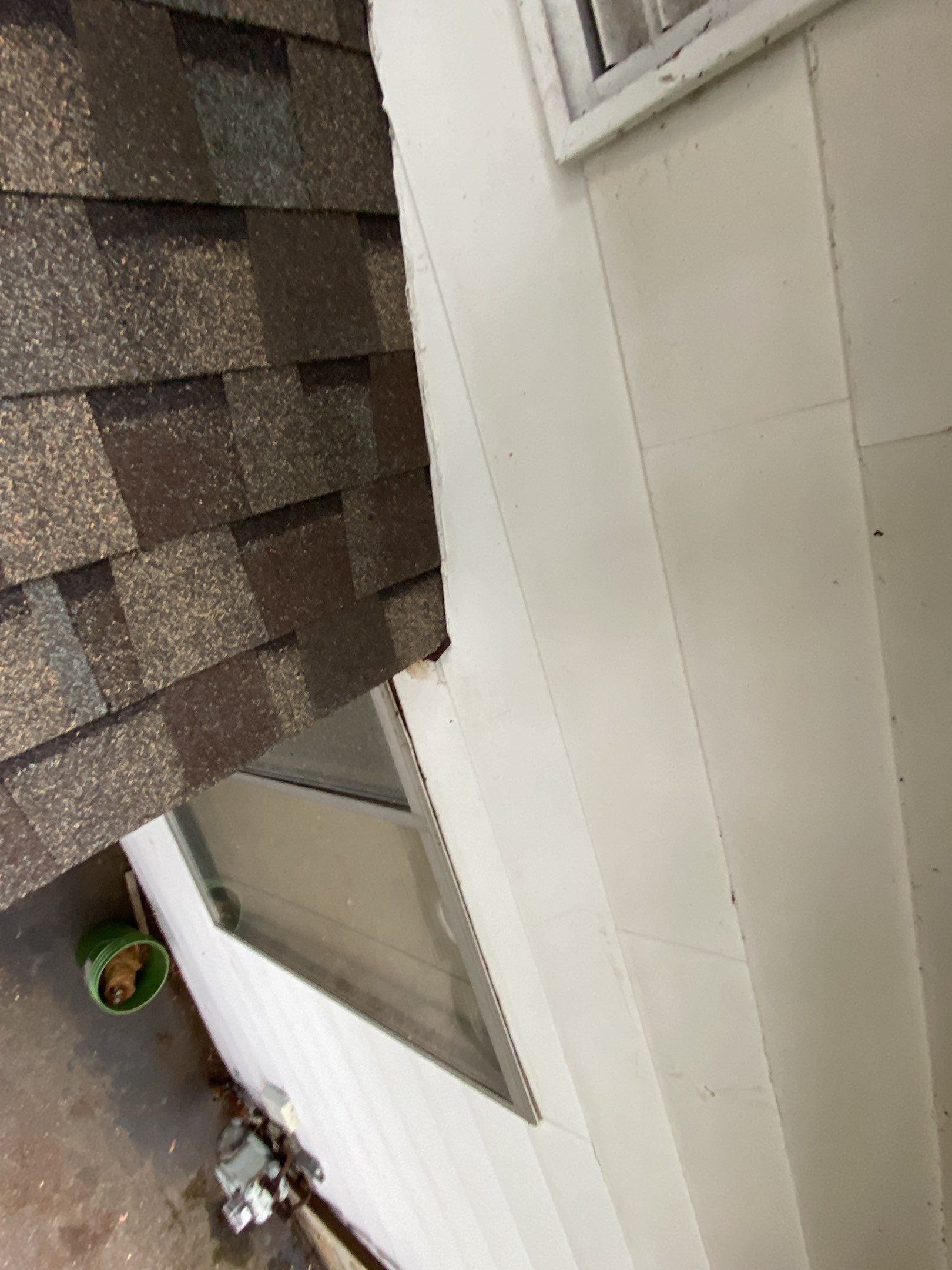 Side of a house with white siding, brown shingle roof, and a narrow concrete walkway below.