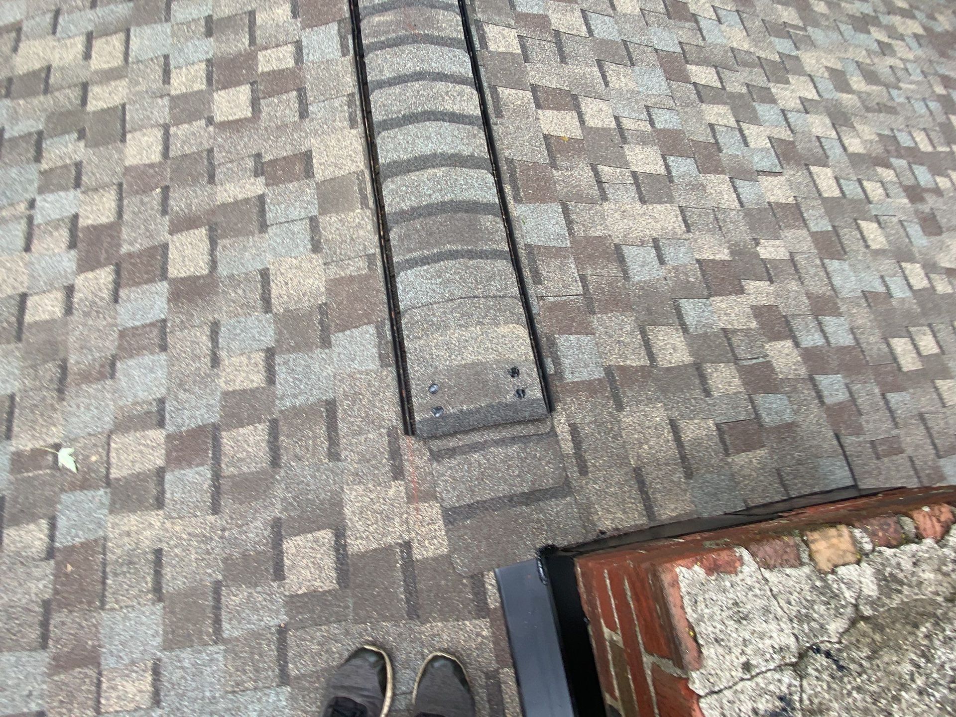 Shoes on a shingled rooftop beside a narrow vent and chimney edge