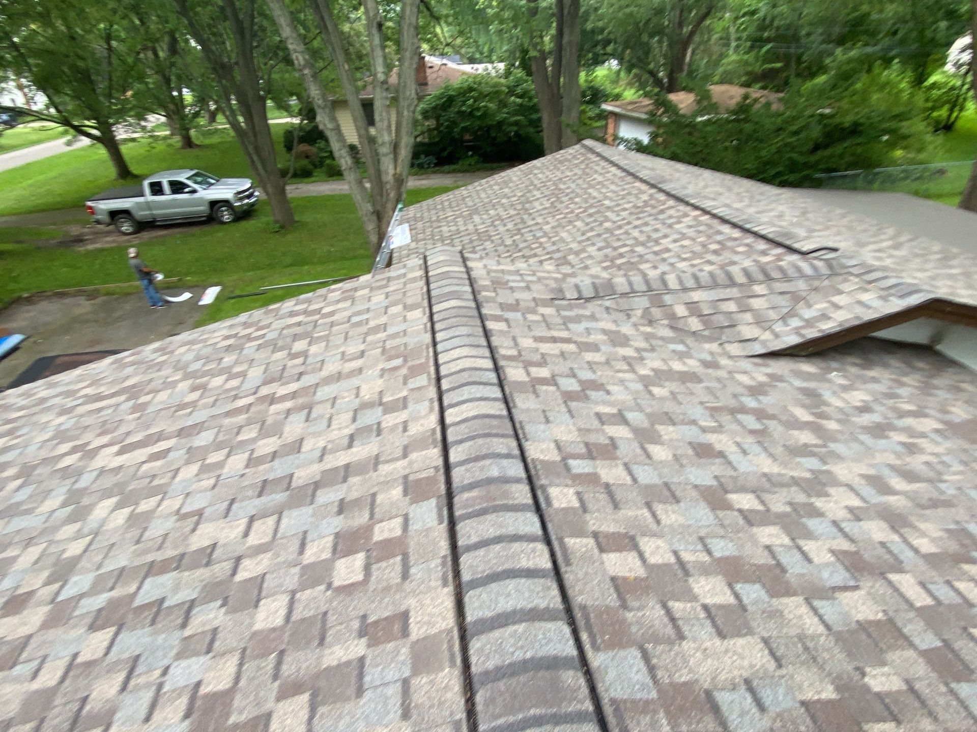 Shingled roof with central ridge vent, viewed over a green suburban yard with a parked truck.