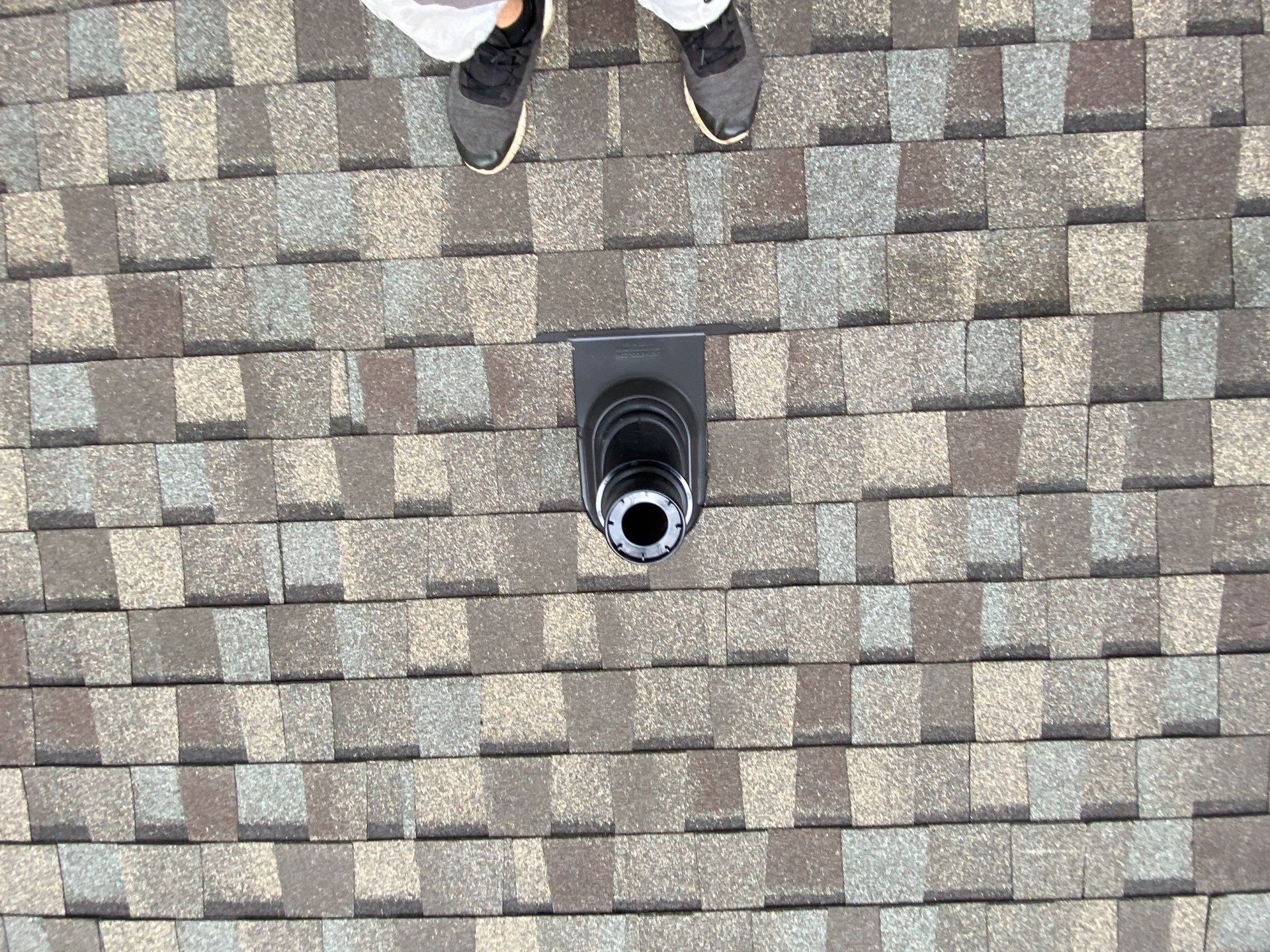 Roof shingles with a small black vent pipe; the tips of two shoes are visible at the top edge.