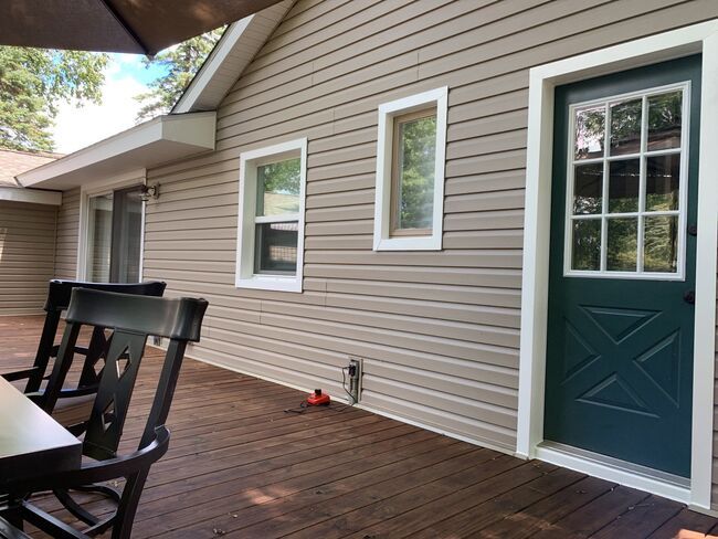 Covered porch with brown siding, wooden deck, and teal door with white-trimmed windows