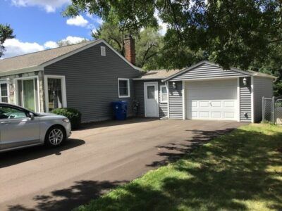 Suburban house with attached garage and driveway, silver car parked outside, trees and lawn in front