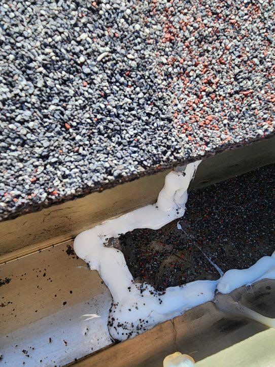 Snow piled along the edge of a roof beside a speckled gravel surface