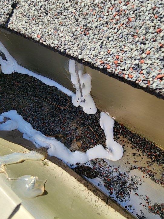White sealant bead along the edge of a gravel roof and tan wall, with a damp corner below.