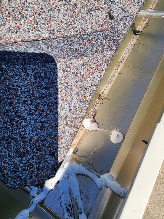 Close-up of a rooftop gutter seam with white sealant and speckled roofing material