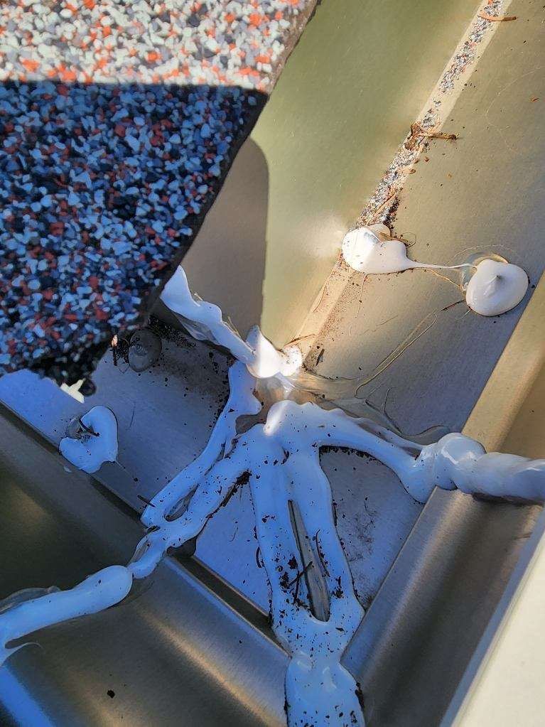 Close-up of white sealant drips on a beige metal surface next to a speckled countertop edge