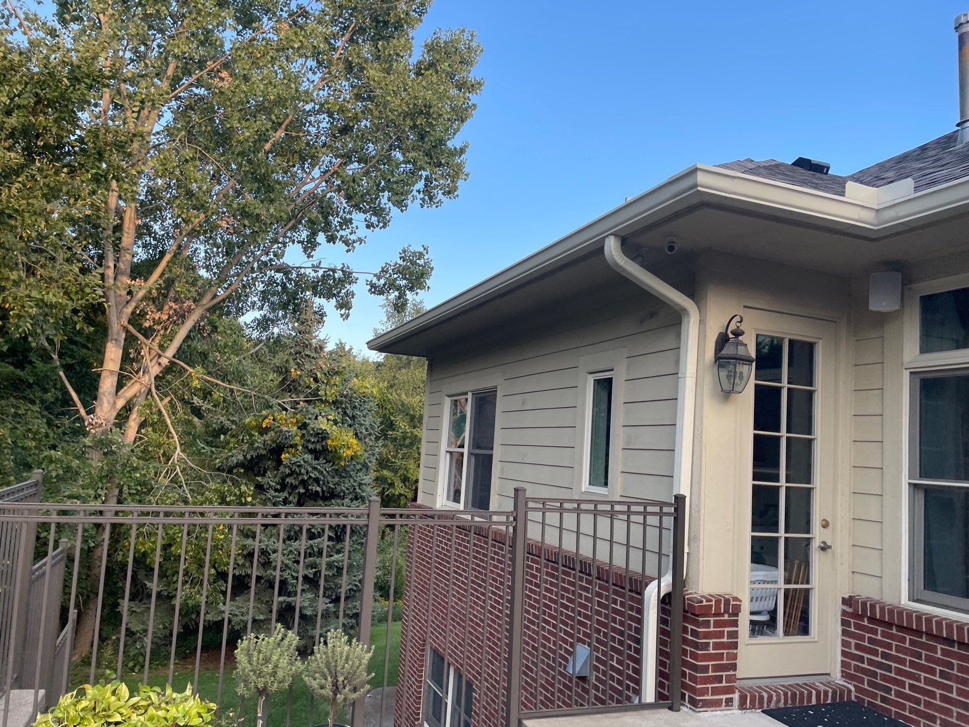 House exterior with covered porch, brick railing, and trees beside a balcony under a blue sky