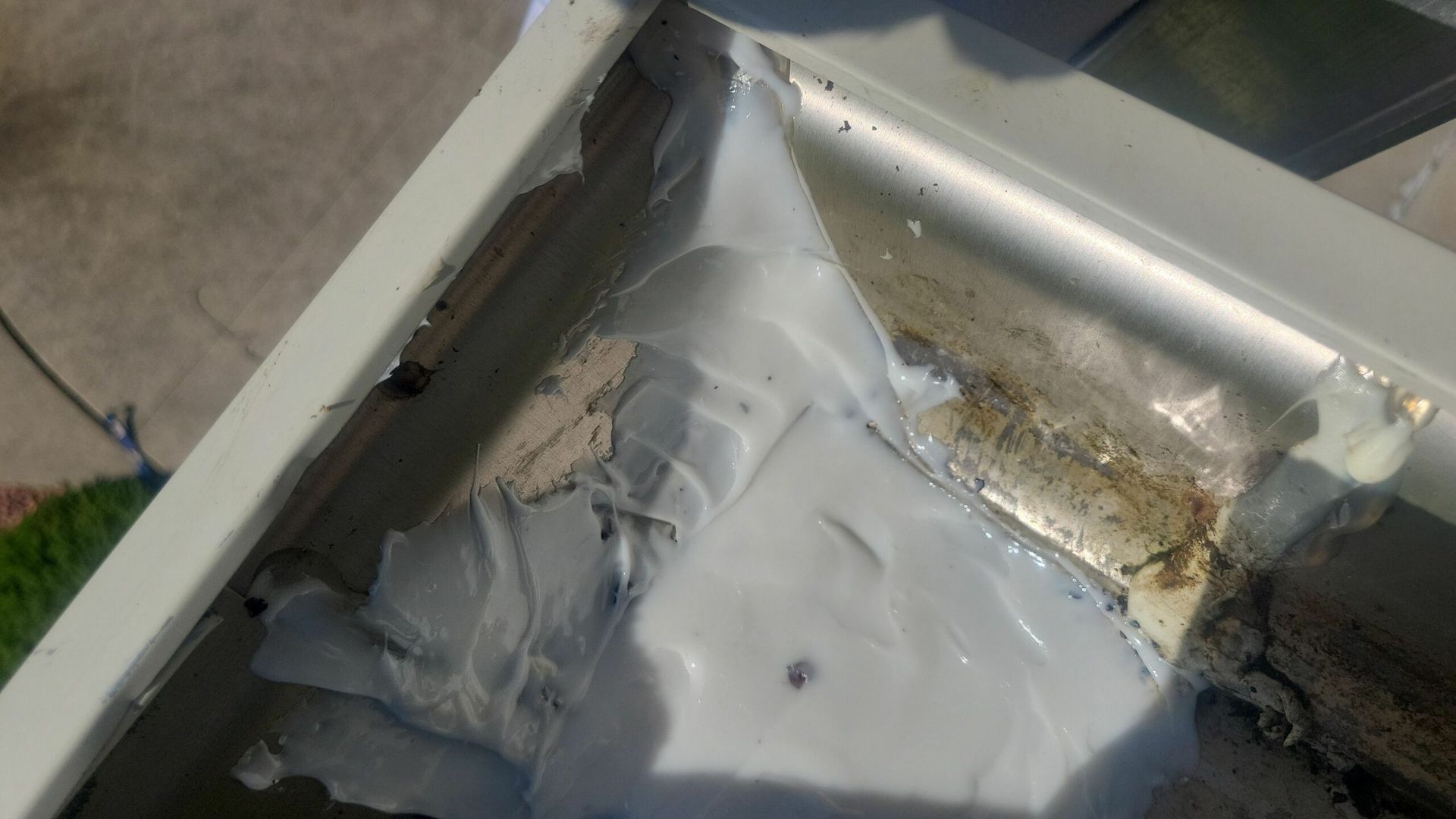 Close-up of a damaged metal roof corner with torn white sealant and debris buildup