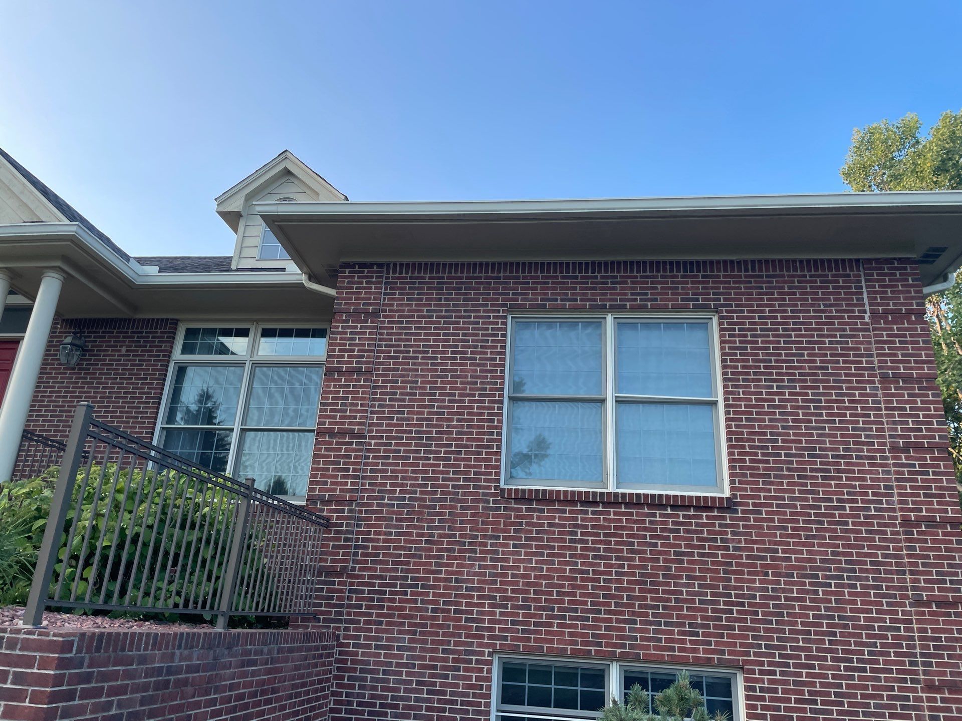 Red brick townhouse exterior with windows, black roof trim, and blue sky above