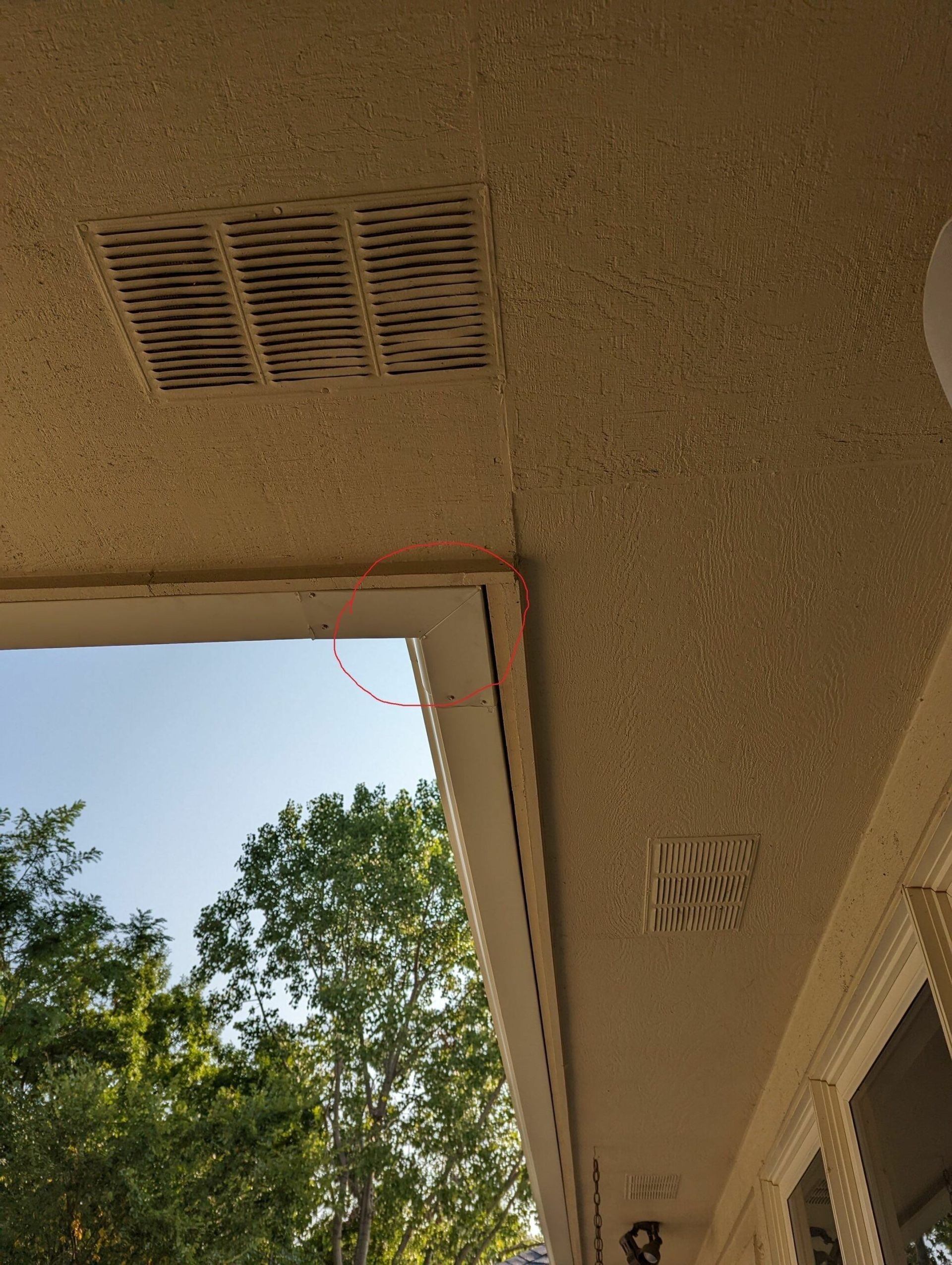 Covered patio ceiling with vents and an open doorway framing trees and blue sky
