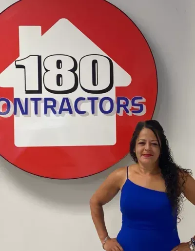Woman in blue dress standing before a red “180 Contractors” wall sign