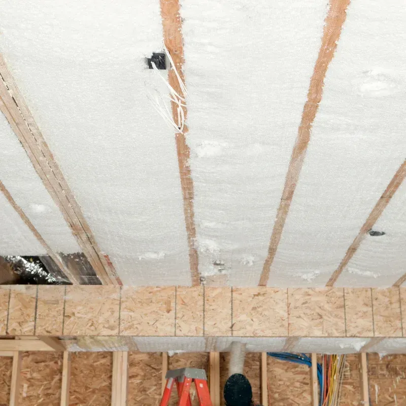 Insulated attic ceiling with exposed wooden rafters and hanging wires above a framed wall